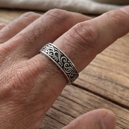 Silver tone band ring with black filigree scrollwork on finger