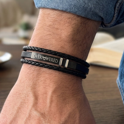 Black leather braided bracelet on wrist with silver clasp and OVERPOWERED logo plate