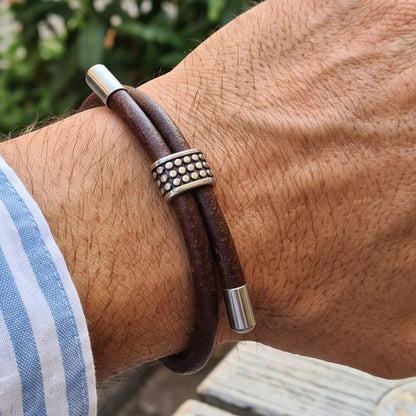 Men's brown leather bracelet on wrist with studded silver ring and silver end bars