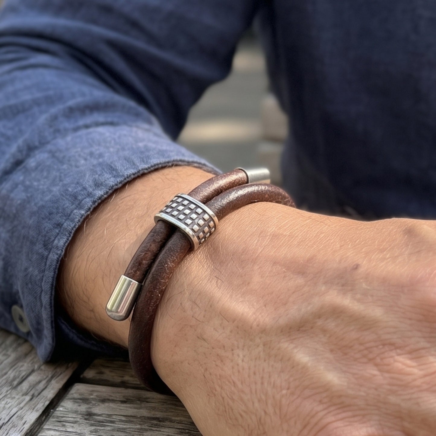 Men's brown leather bracelet on forearm with studded silver center and cylindrical end caps