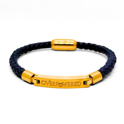 A braided navy blue cord bracelet with polished gold-toned metal accents, including a central bar engraved with the word 'OVERPOWERED'.