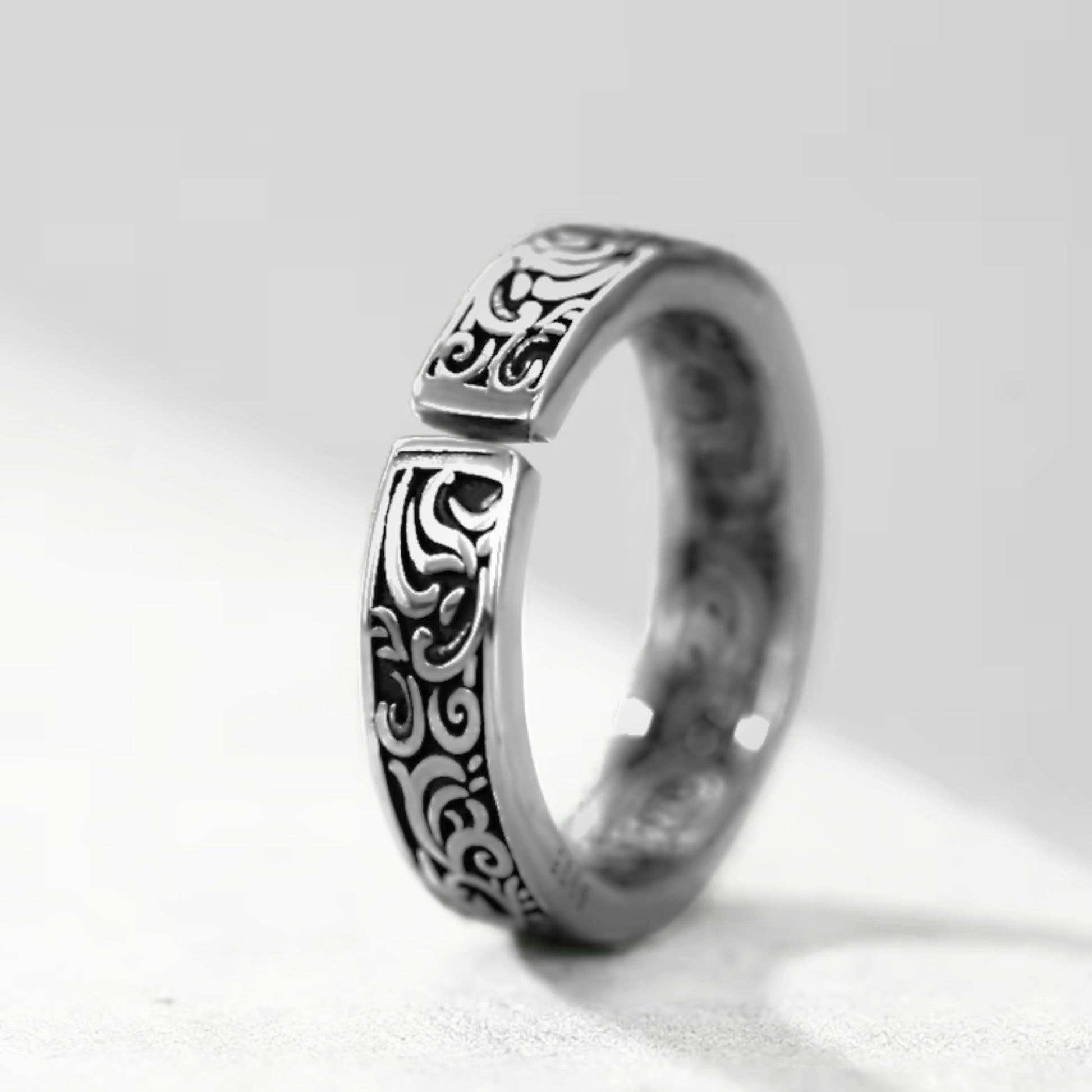 Silver tone ring with ornate black swirling pattern on the top edge