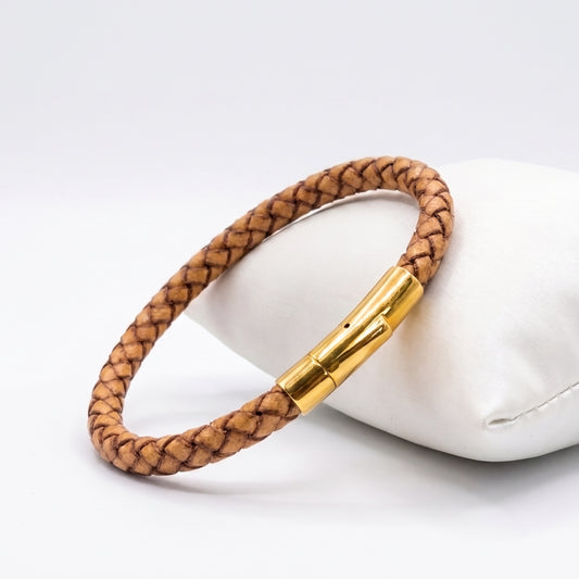 Light brown braided leather bracelet with gold-tone clasp on white cushion
