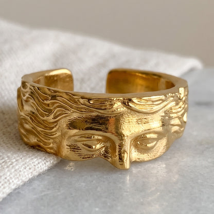 Gold sculpted face ring angled view showing symmetrical facial features and hair