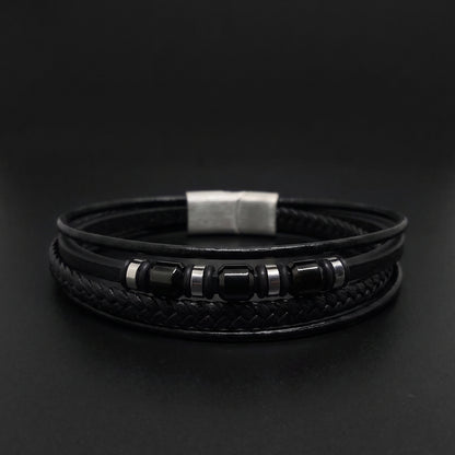A black multi-strand leather bracelet featuring a braided center band, a silver-toned rectangular clasp, and smooth black beads with silver spacer rings, displayed on a dark background.