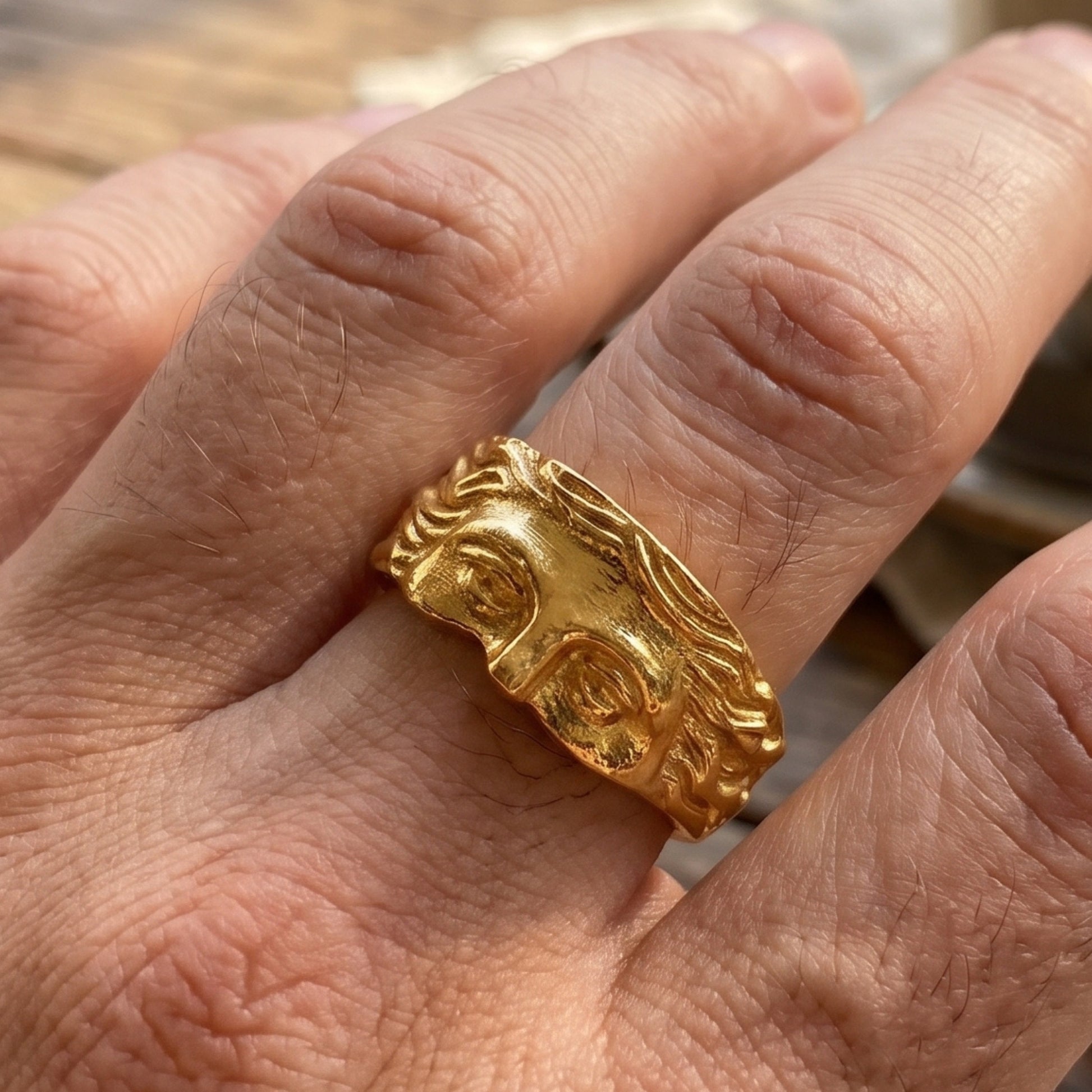 Gold sculpted face ring on hand, wide band with raised eyes and hair relief