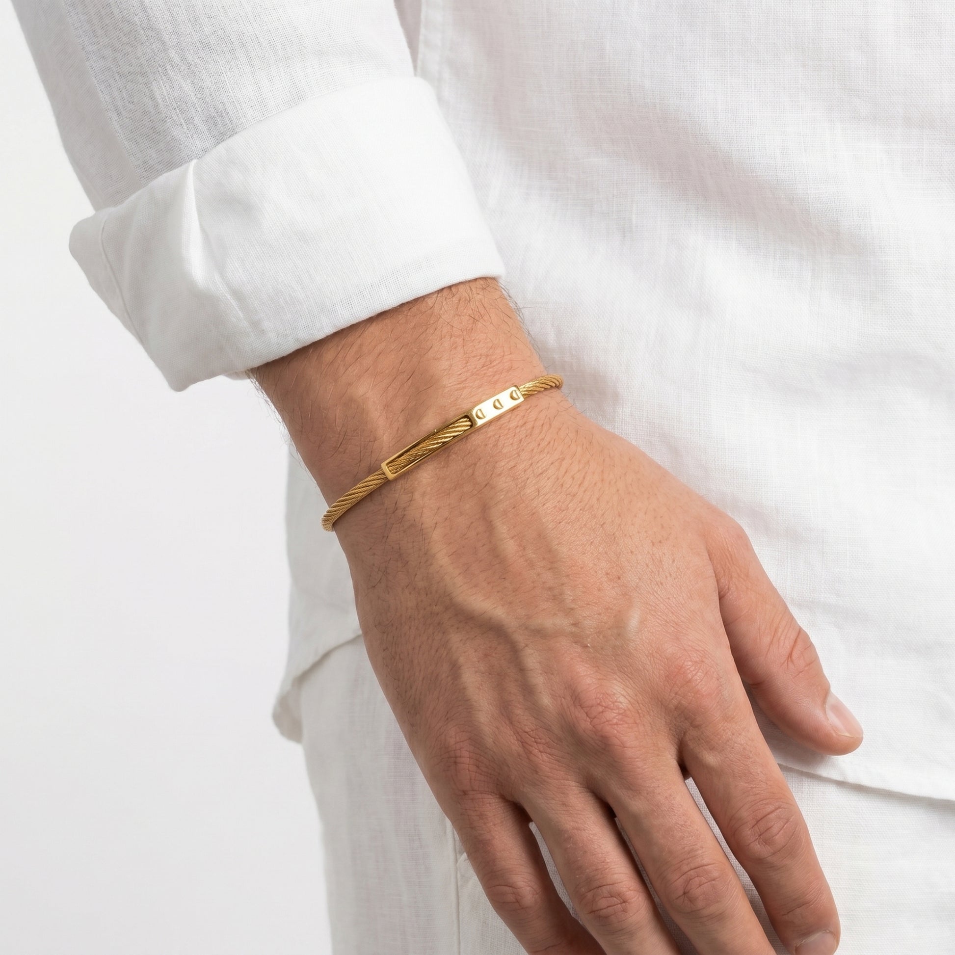 Gold bracelet on a person's wrist with a white shirt background