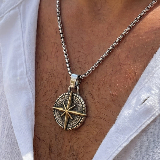 Two-tone compass pendant necklace on chest: dark round dial with gold compass rose, silver chain