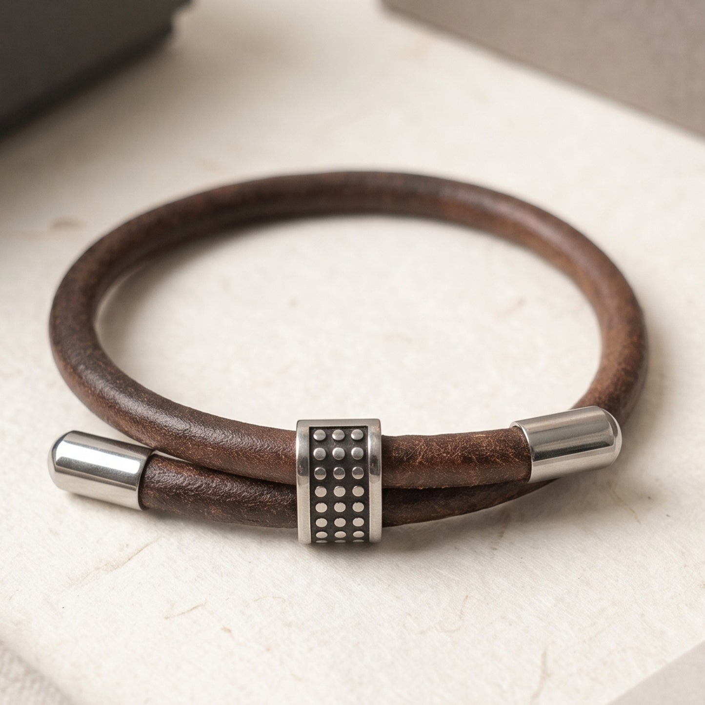 Men's brown leather bracelet on light surface, studded center and silver end caps