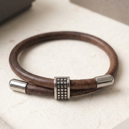 Men's brown leather bracelet on light surface, studded center and silver end caps