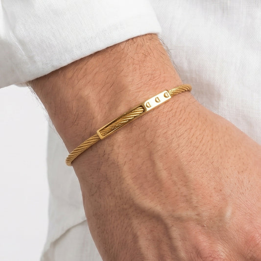 Gold bracelet on a wrist with a plain background