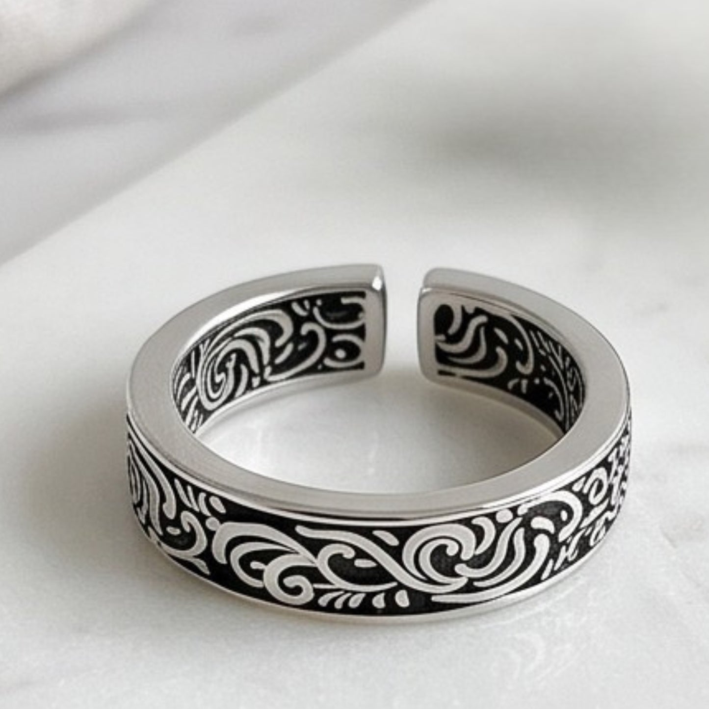 Silver tone ring with black scrollwork details on the band