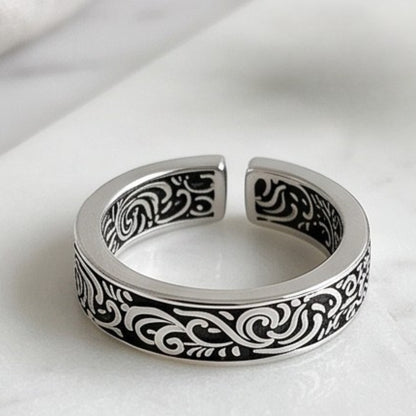 Silver tone ring with black scrollwork details on the band