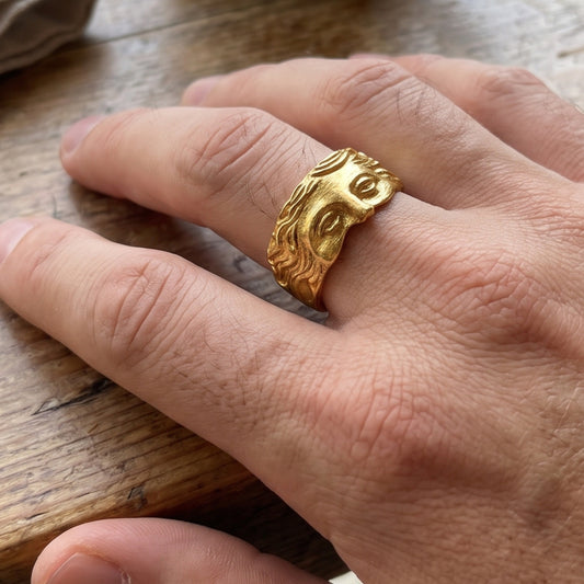 Gold sculpted face ring on hand, close view of sculpted face relief on band