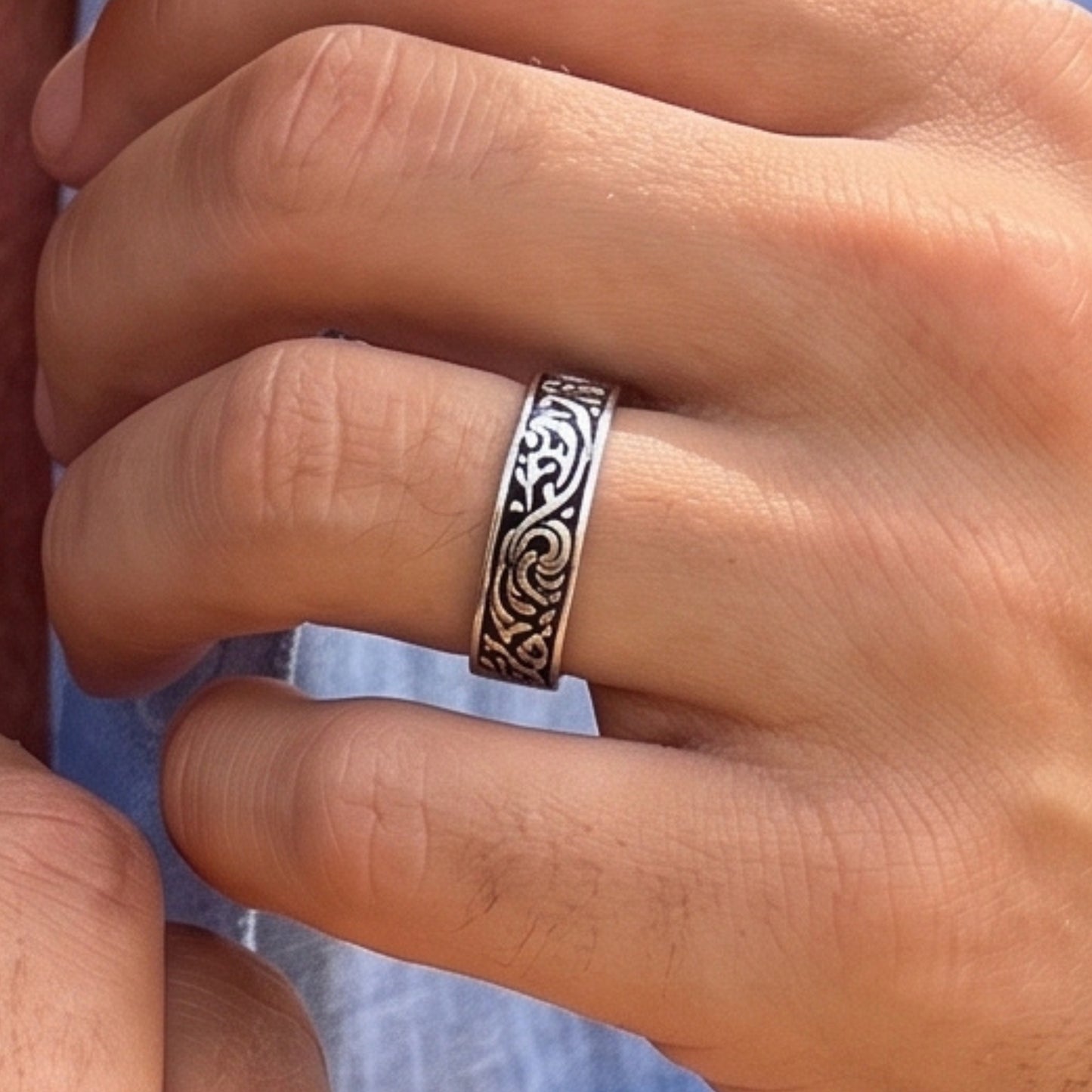 Silver tone ring with black scrollwork worn on a finger