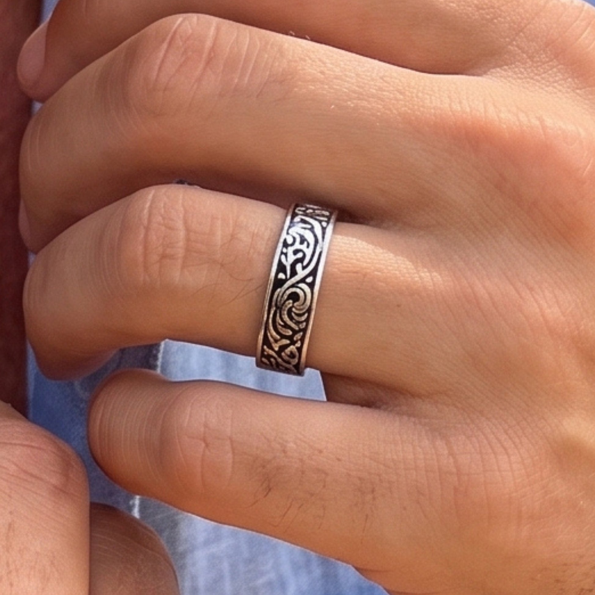 Silver tone ring with black scrollwork worn on a finger