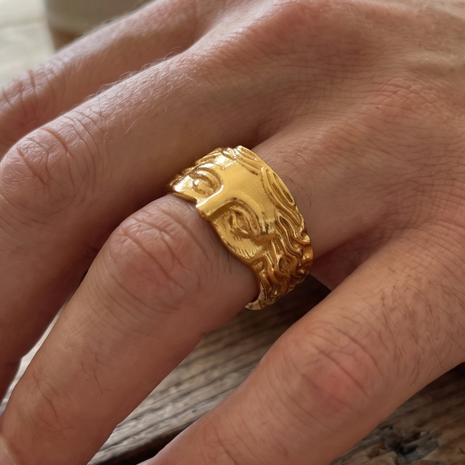 Gold sculpted face ring on hand, side profile showing relief hair and brow