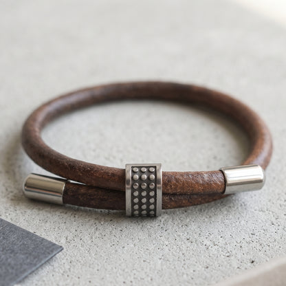 Men's brown leather bracelet with studded metal centerpiece and silver cylindrical end caps