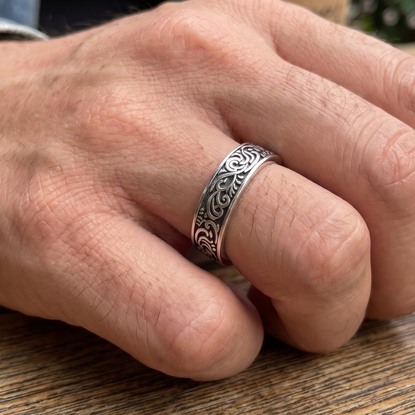 Silver tone men’s ring with black filigree band on an open hand