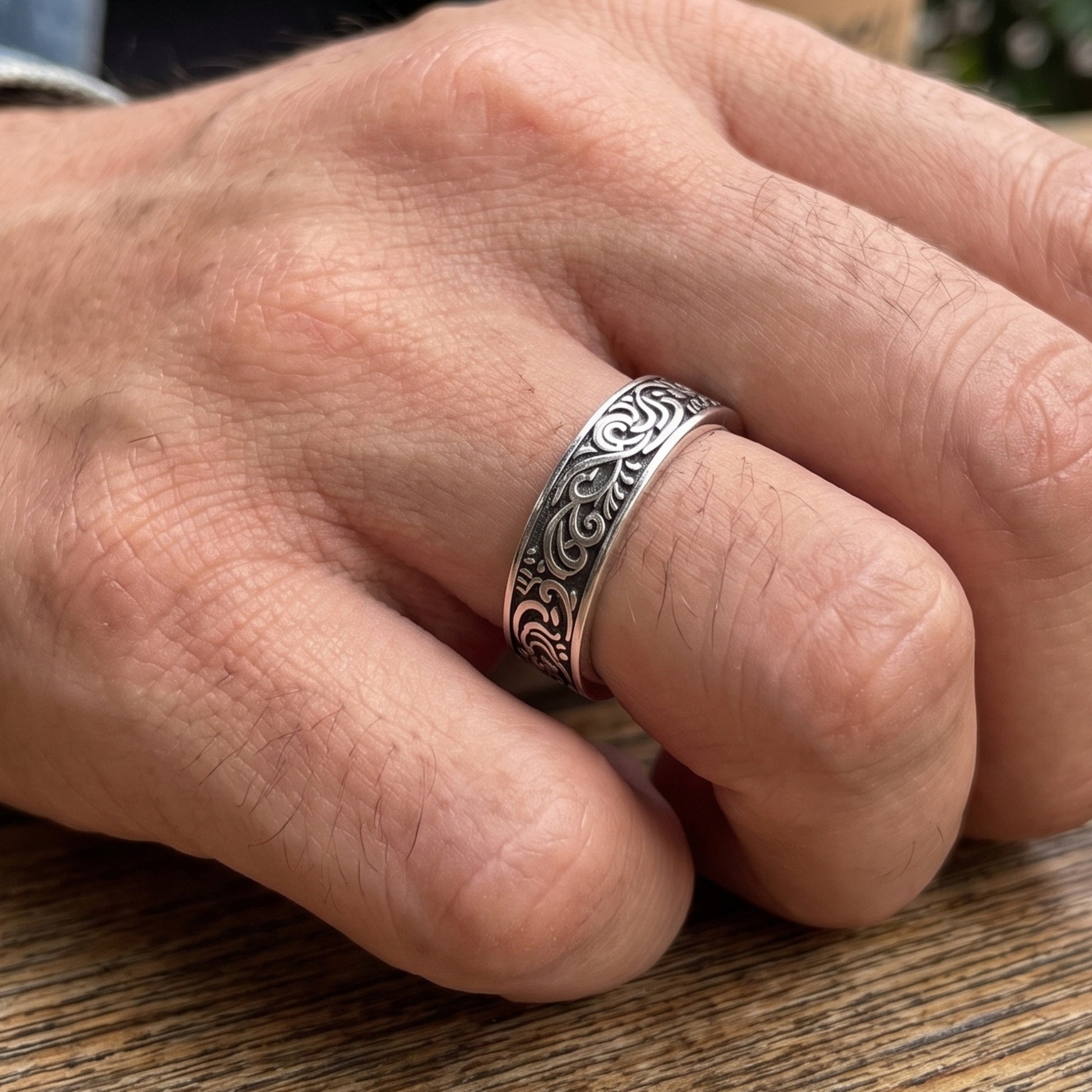 Silver tone men’s ring with black filigree band on an open hand