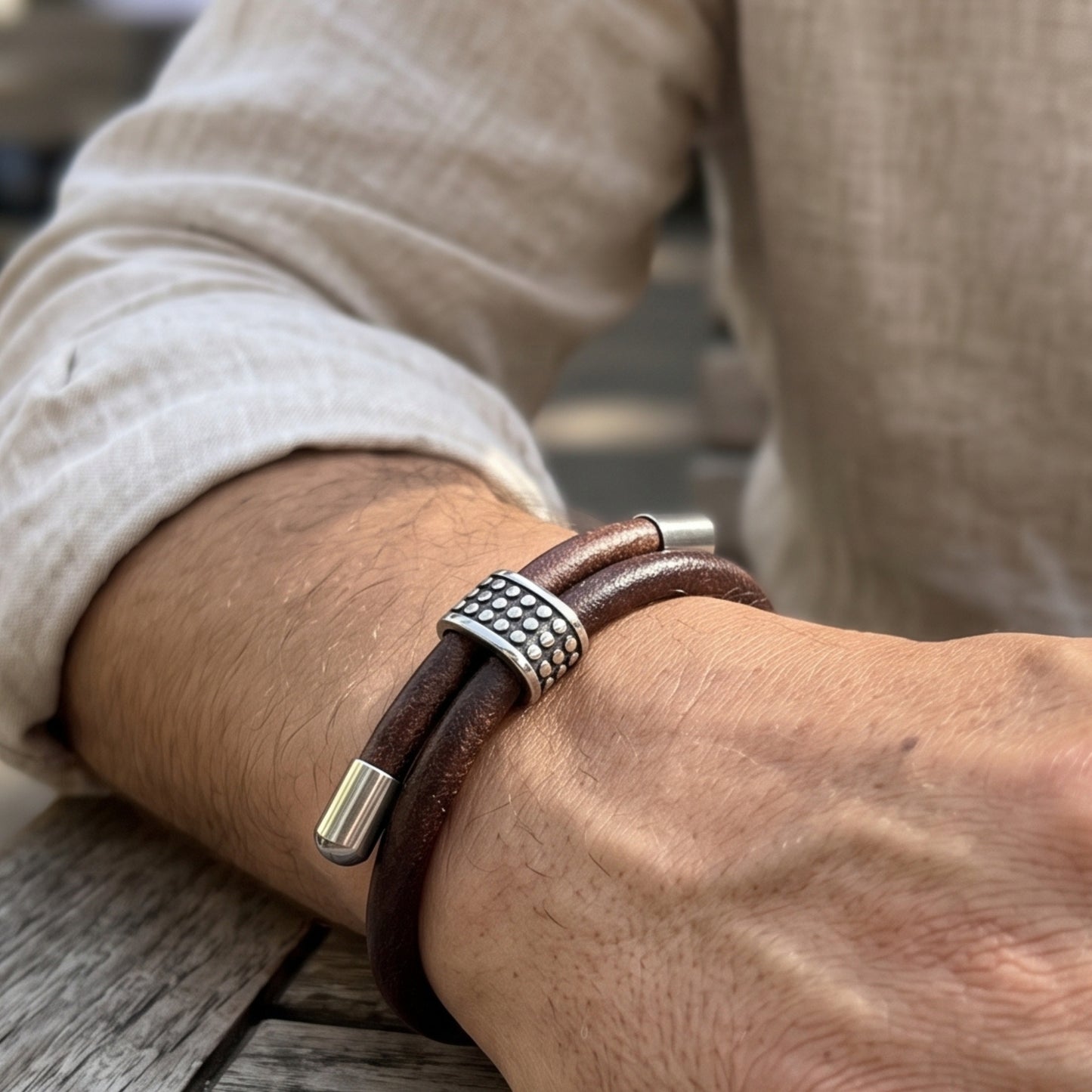 Men's brown leather bracelet on arm with studded silver centerpiece and silver end caps