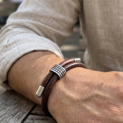 Men's brown leather bracelet on arm with studded silver centerpiece and silver end caps
