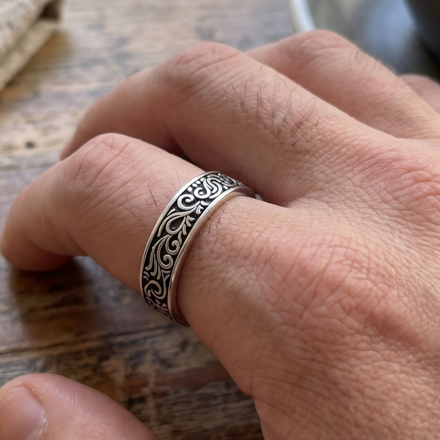 Silver tone ring with black ornate scroll pattern on fingertip