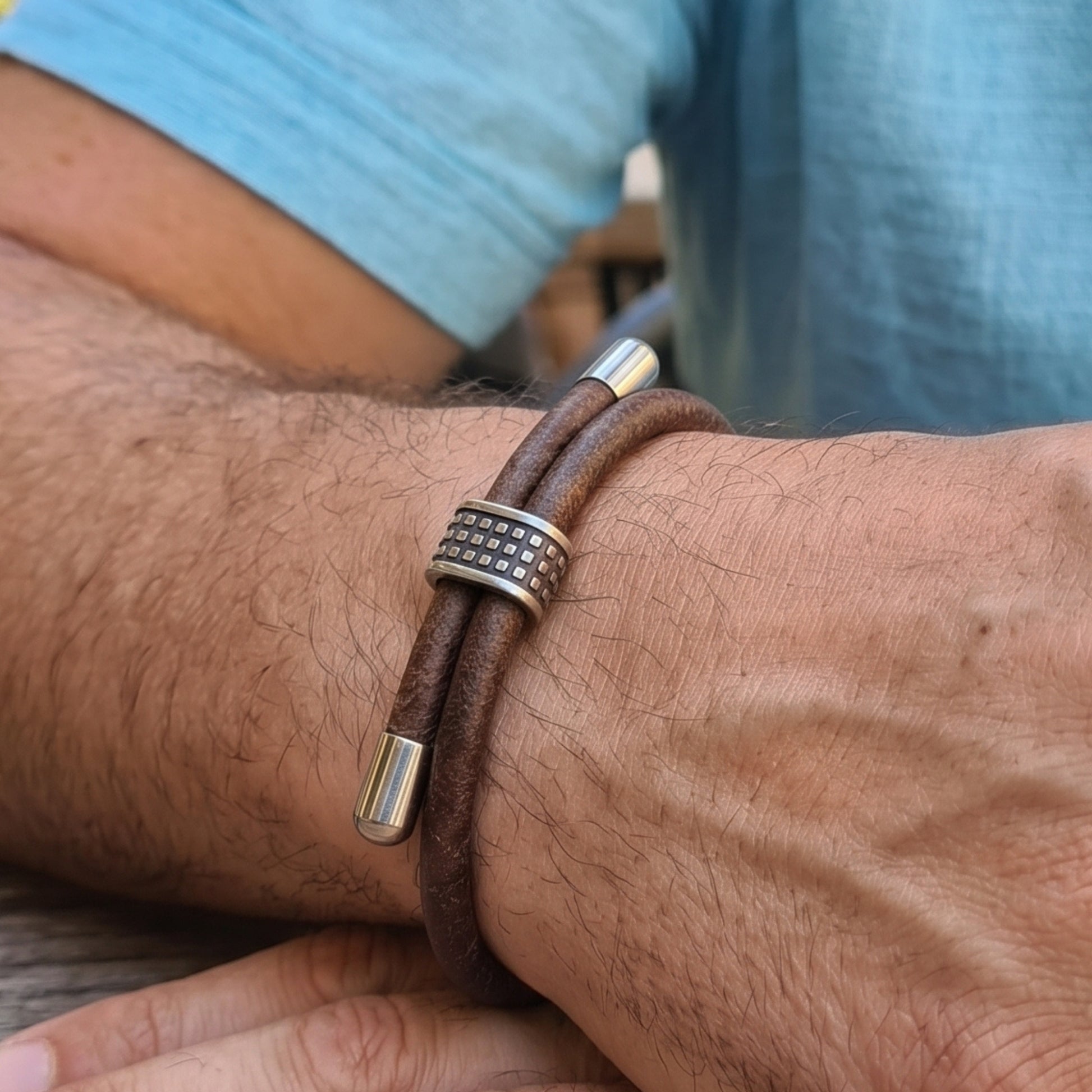 Men's brown leather bracelet on wrist with studded silver center and barrel end caps
