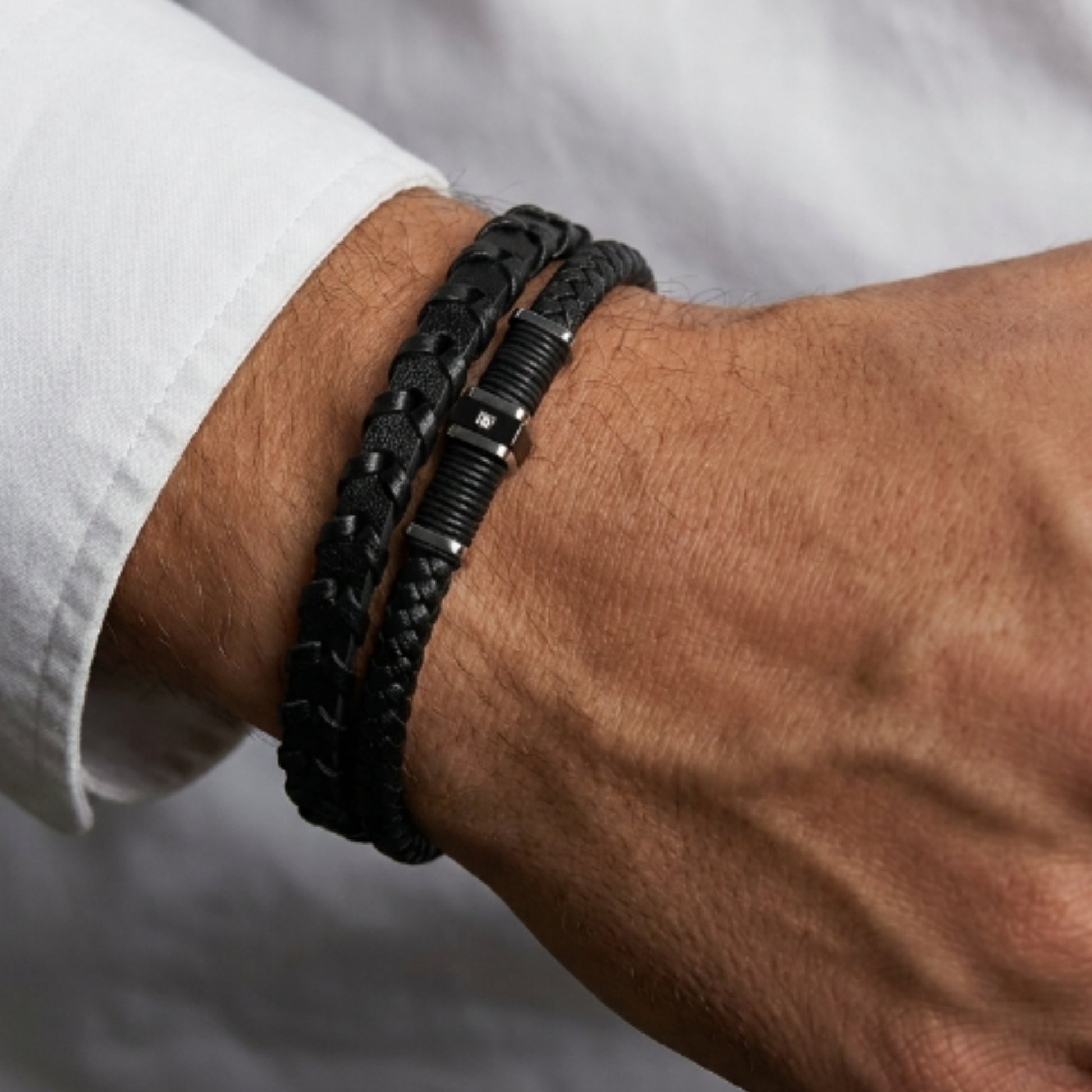 Close-up: men's braided leather bracelet on wrist, black cord with dark metal links