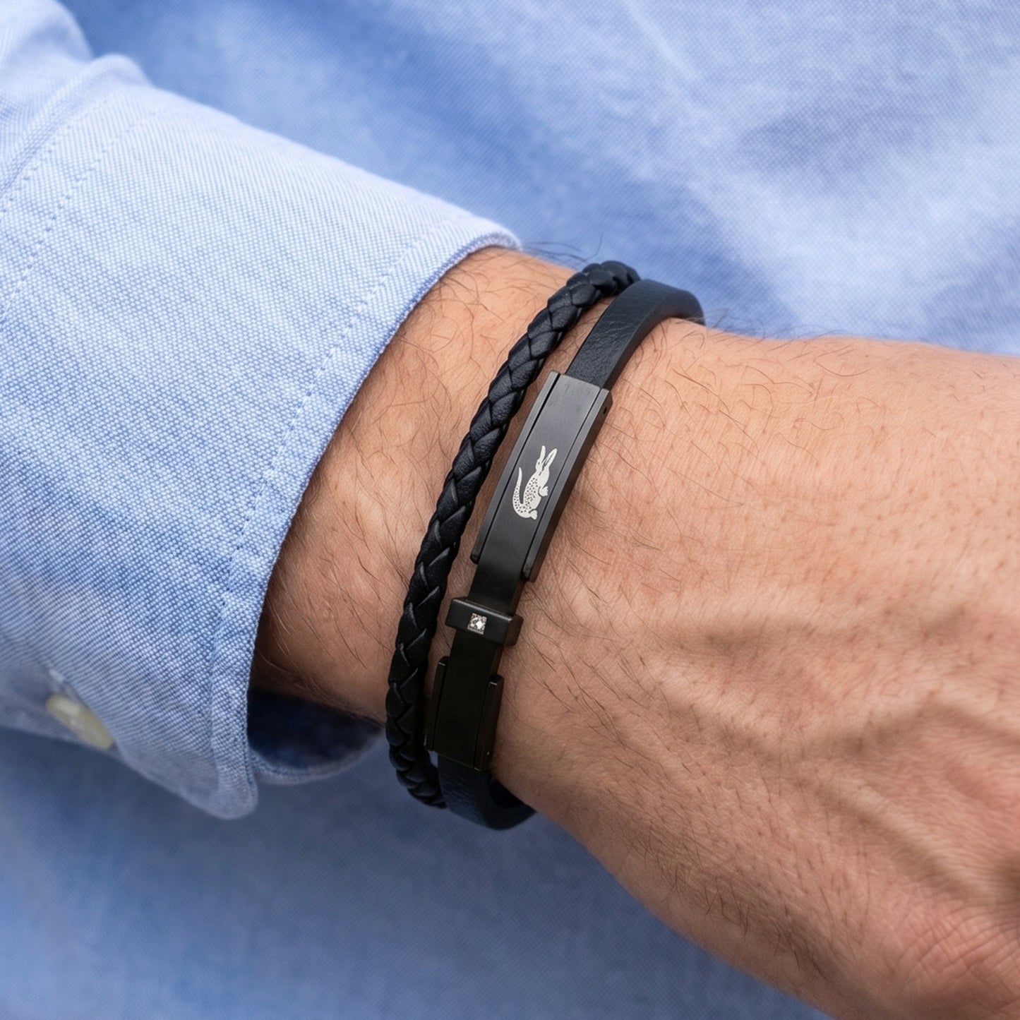 Men's black leather braided bracelet on wrist with metal clasp and logo