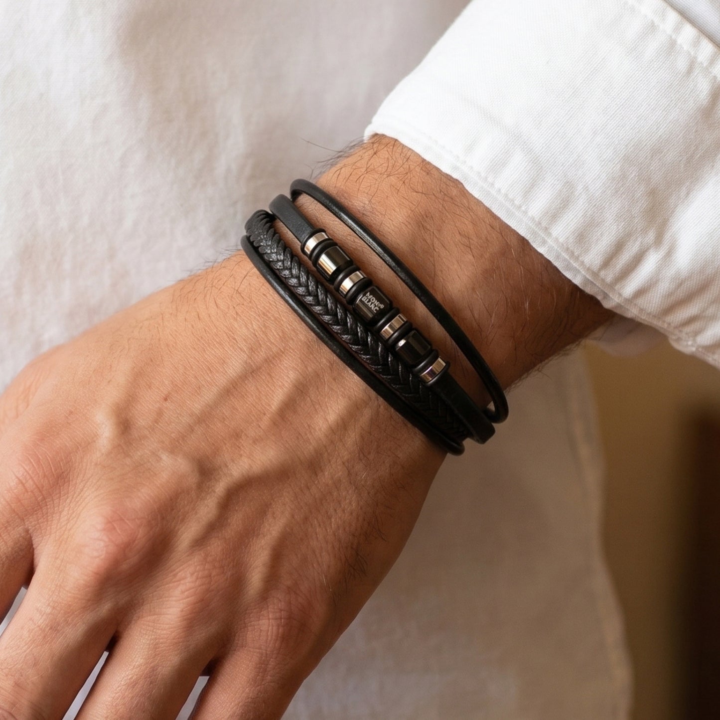 Men's wrist wearing black leather wrap bracelet with metal clasp and logo bead accents