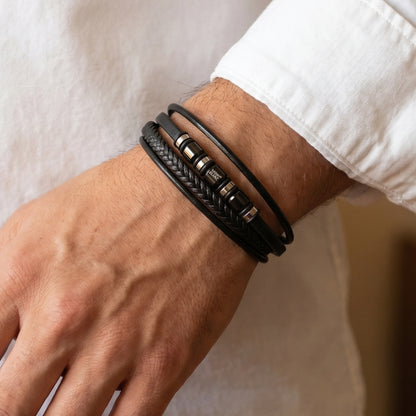 Men's wrist wearing black leather wrap bracelet with metal clasp and logo bead accents
