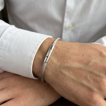 Silver stainless steel bracelet with magnetic clasp, worn on a man's wrist, featuring a sleek cable design.