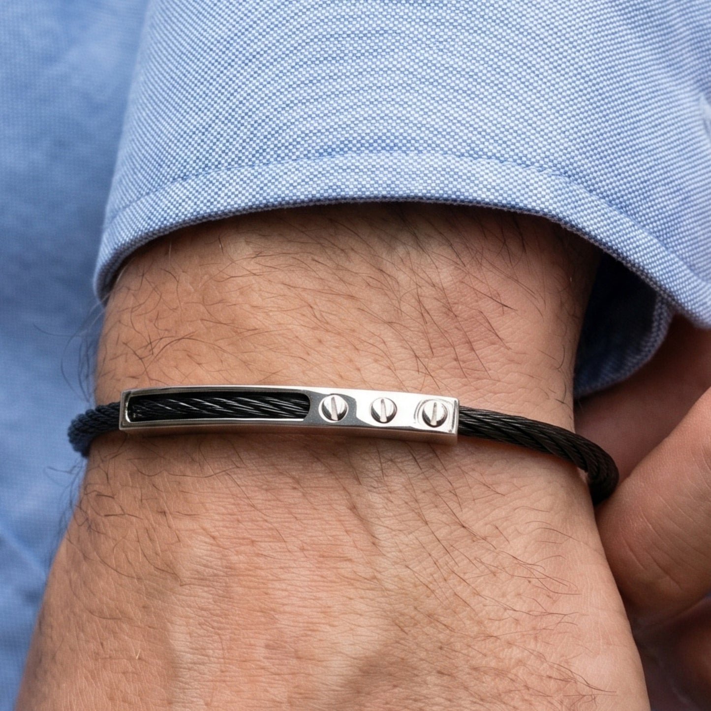 Silver bracelet with black cord on a wrist against a blue shirt background