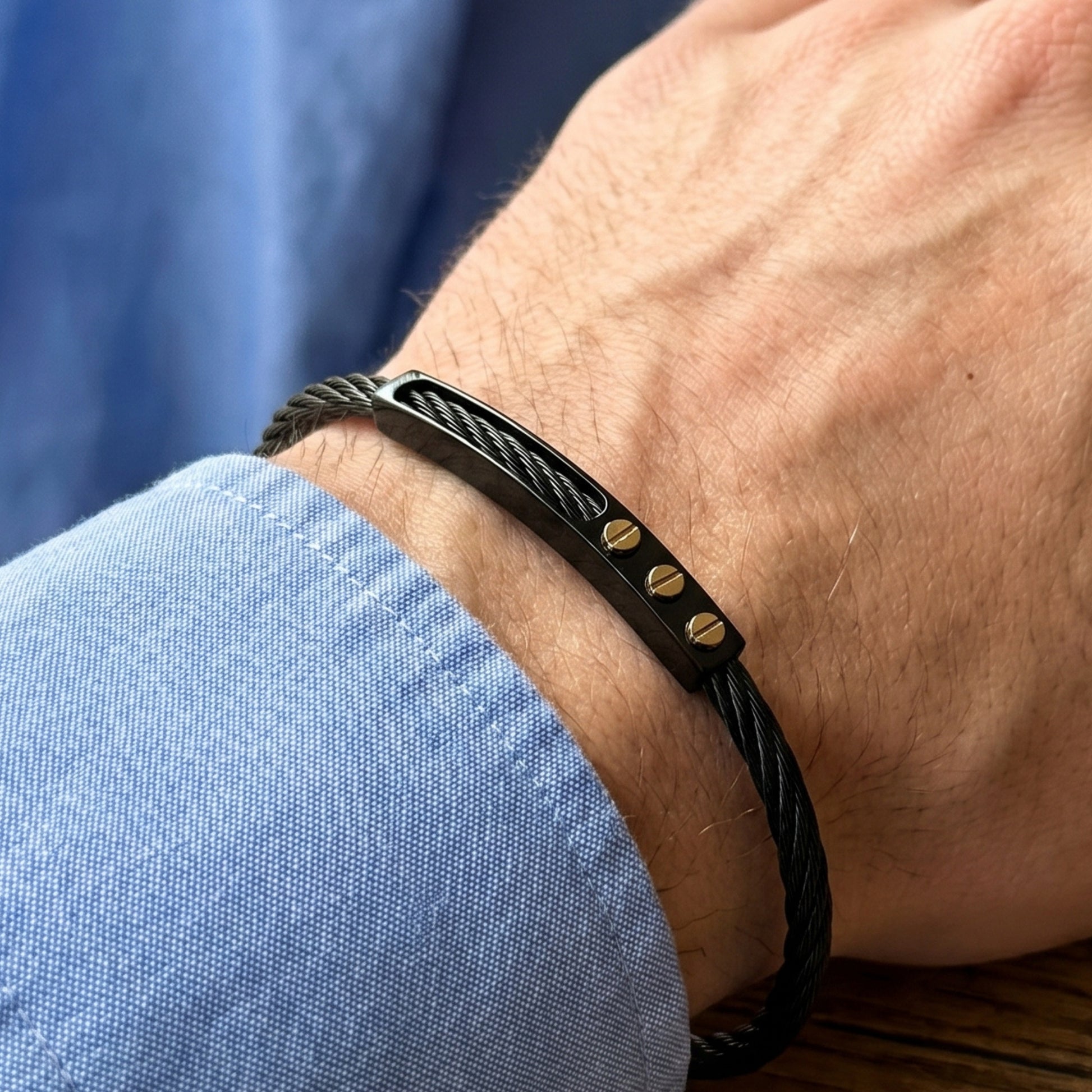 Black braided bracelet with gold accents on a wrist against a blue shirt background