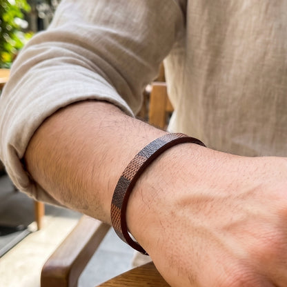 Leather bracelet on arm: brown leather cuff with navy-orange woven texture and black clasp
