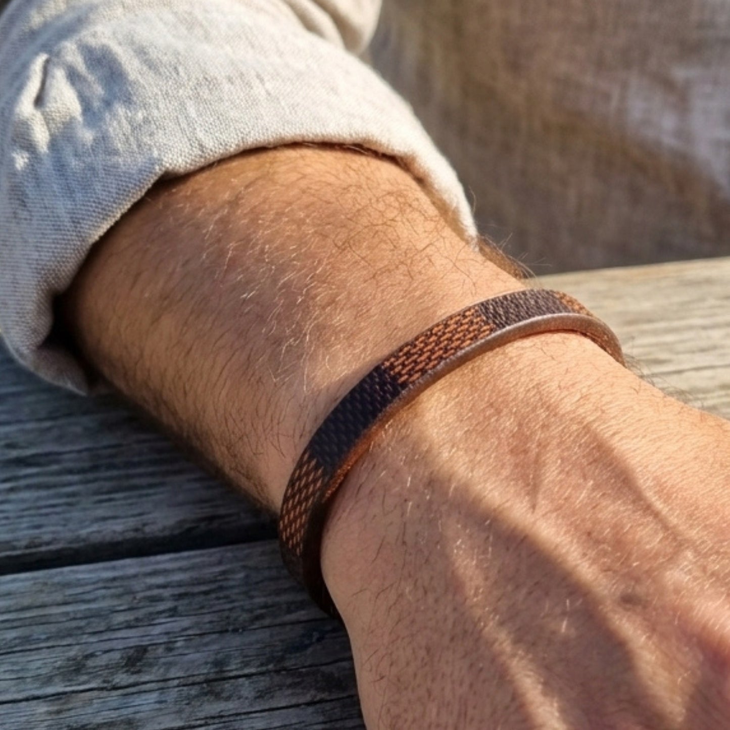 Leather bracelet on wrist: brown strap with navy-orange woven band and black buckle