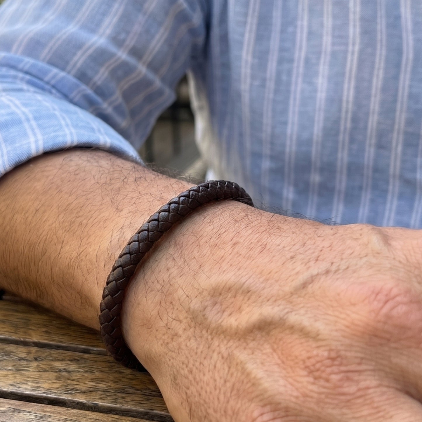 Braided leather bracelet on forearm, dark brown weave and metal clasp visible