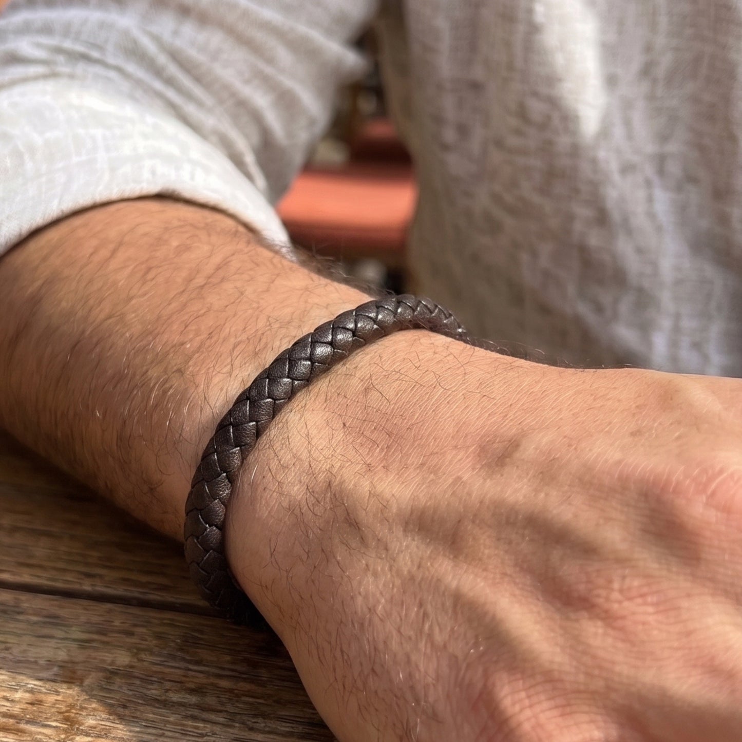 Braided leather bracelet worn on arm, dark brown band with clasp and logo