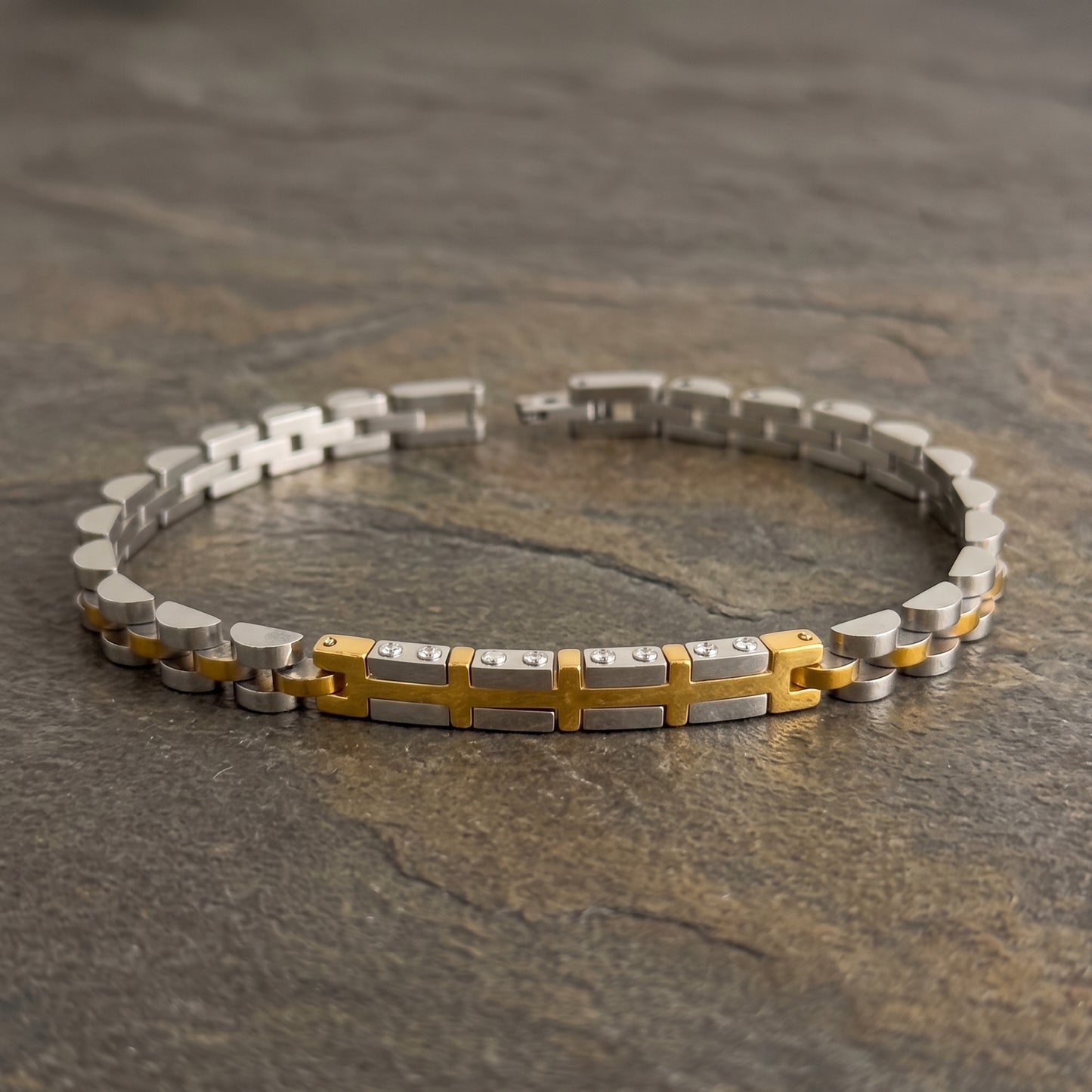 Two-tone silver and gold stainless steel bracelet with central cross pattern, flat lay