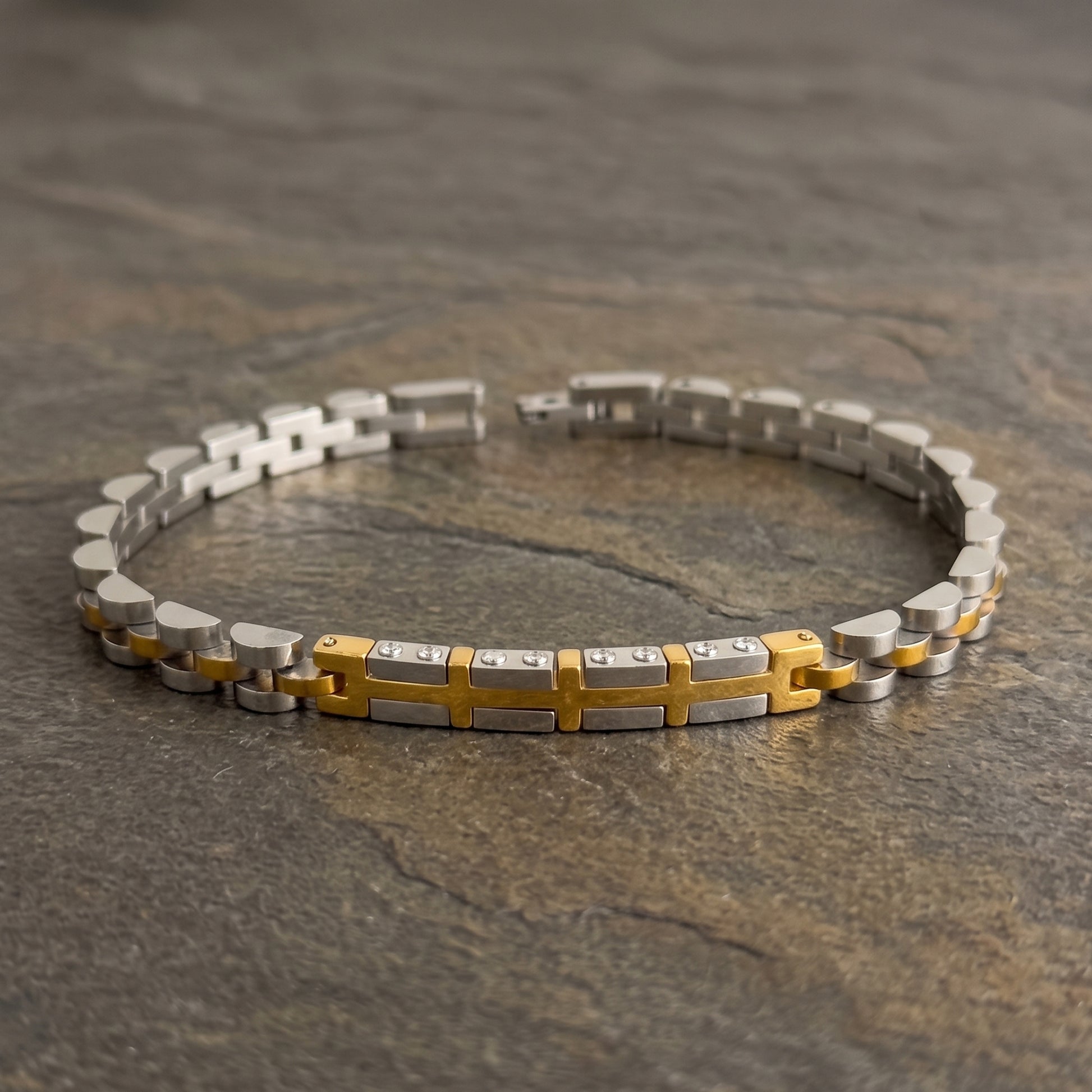 Two-tone silver and gold stainless steel bracelet with central cross pattern, flat lay