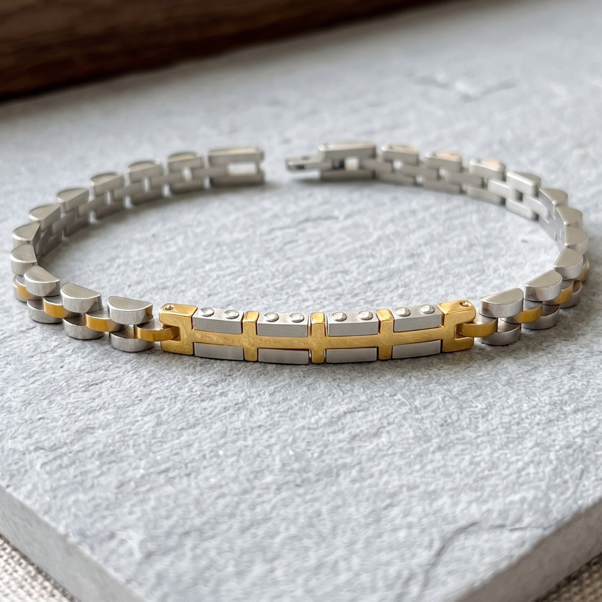 Two-tone silver and gold link bracelet with gold center cross on display base
