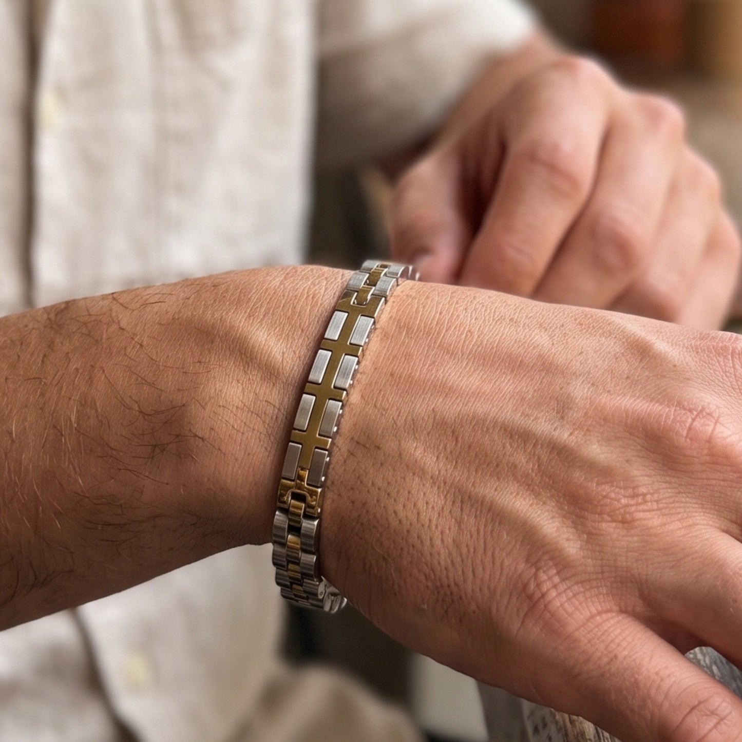 Two-tone silver and gold stainless steel bracelet on wrist with link and cross detail