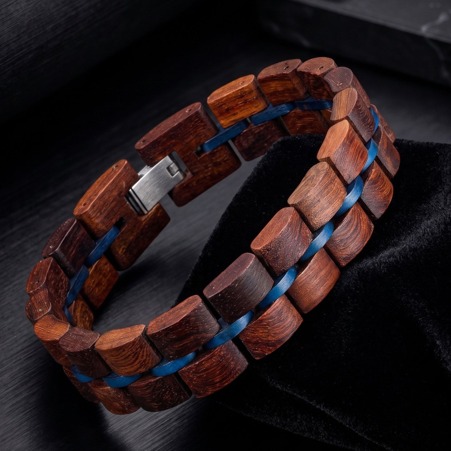 A wooden link bracelet made of dark reddish-brown wood links with a blue inlay, featuring a silver metal clasp, displayed on a black velvet surface.