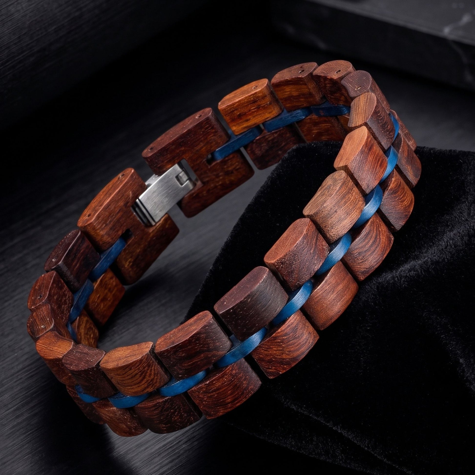 A wooden link bracelet made of dark reddish-brown wood links with a blue inlay, featuring a silver metal clasp, displayed on a black velvet surface.