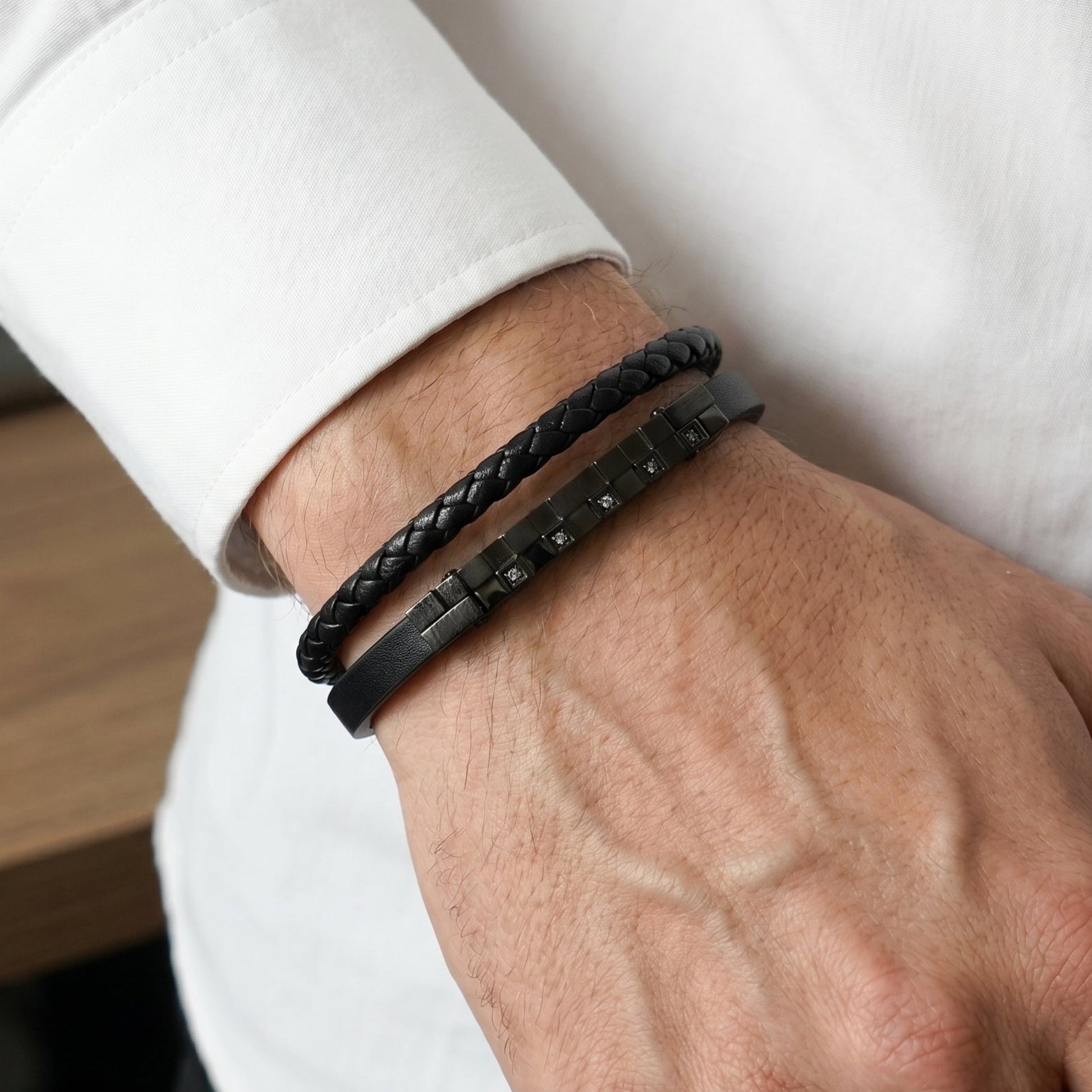 Men's black leather bracelet on arm, braided strap and dark square-studded zircon bar.
