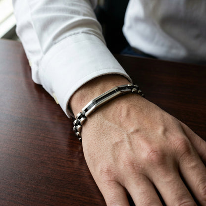 Two-tone silver and black stainless steel B-84 bracelet worn on a man's wrist, showcasing a stylish design.