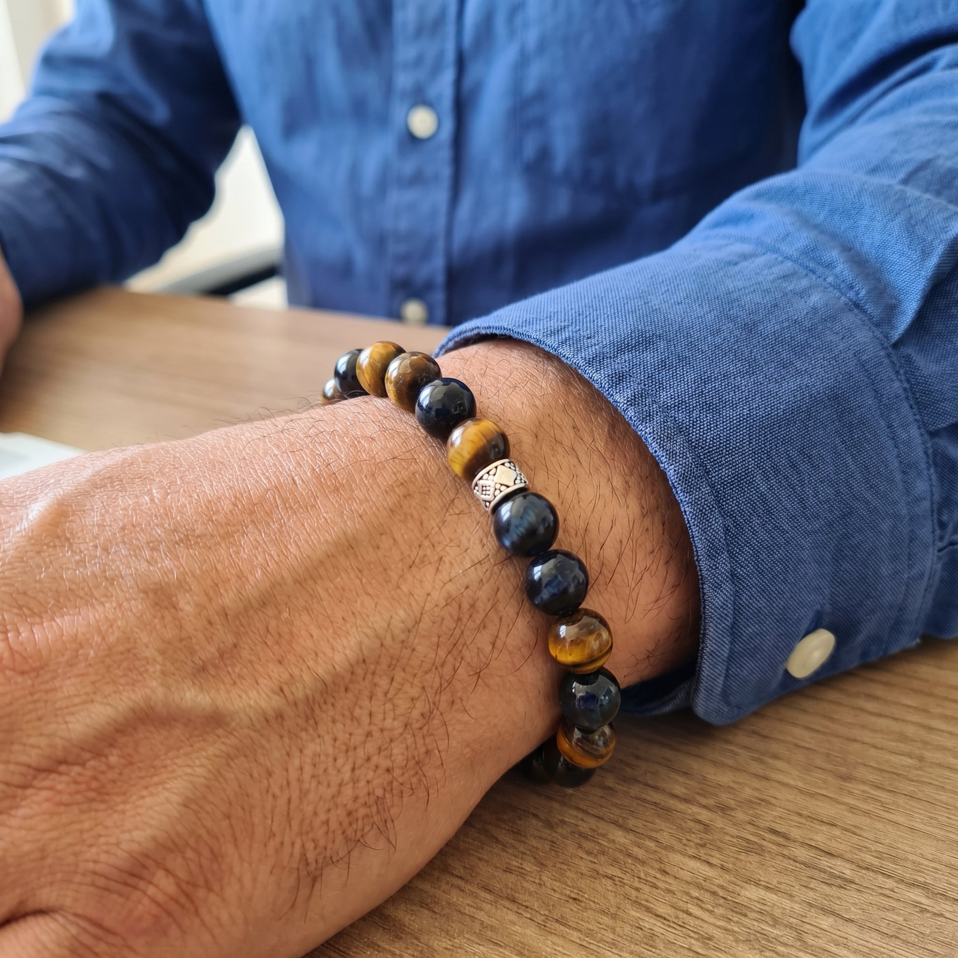 Mens bracelet on wrist: dark navy and amber tiger eye beads with silver geometric center charm