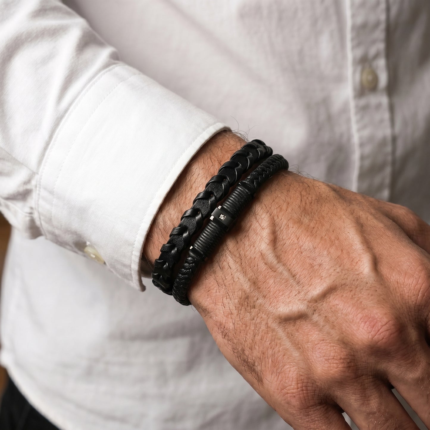 Men's black braided leather bracelet worn on forearm with micro-zircon clasp detail