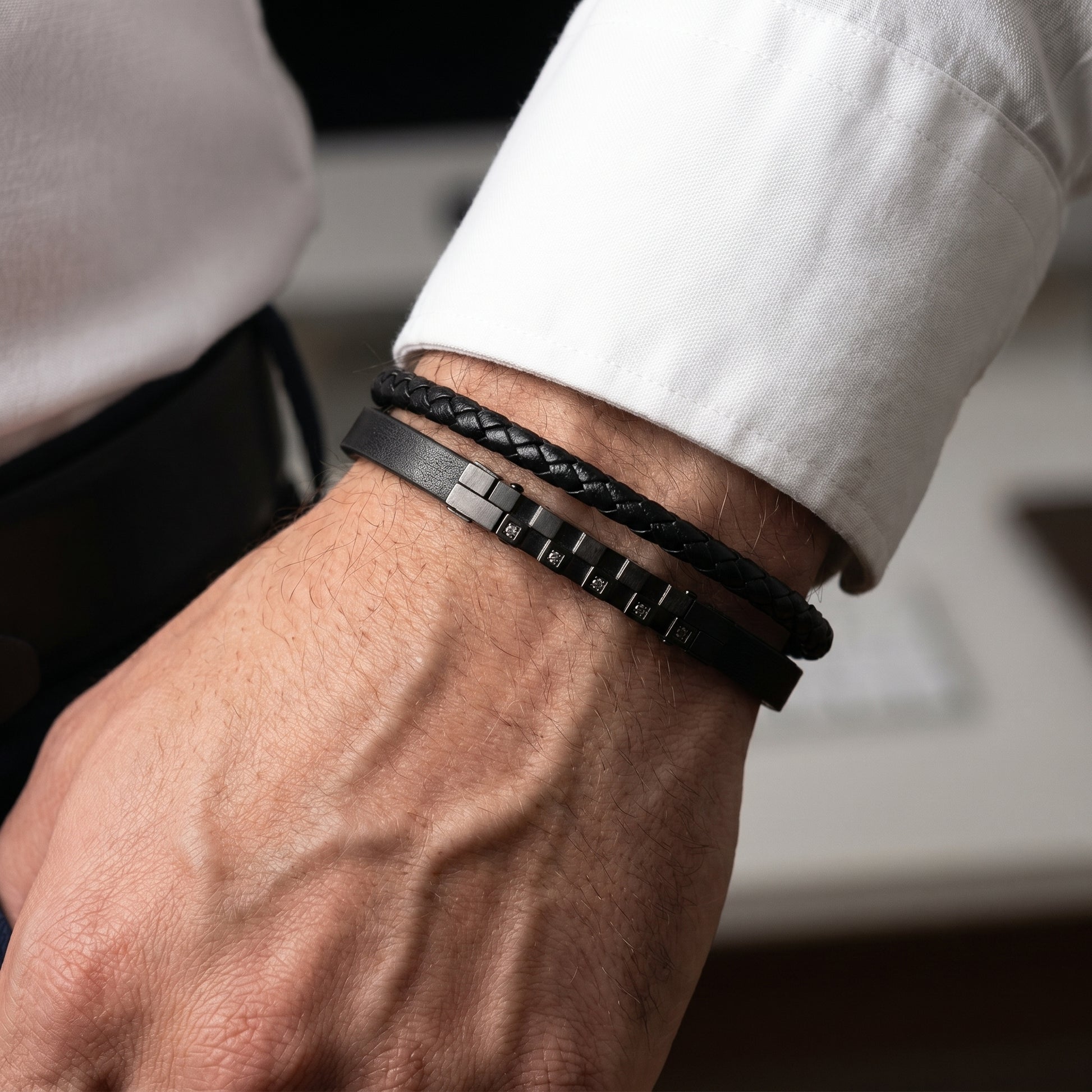 Men's black leather bracelet set on wrist, braided cuff with dark studded zircon strip.